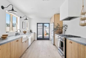 Scandinavian style double galley kitchen with light wood cabinets and black fixtures.